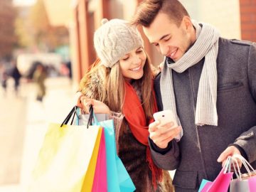 Happy couple shopping in the city with smartphone